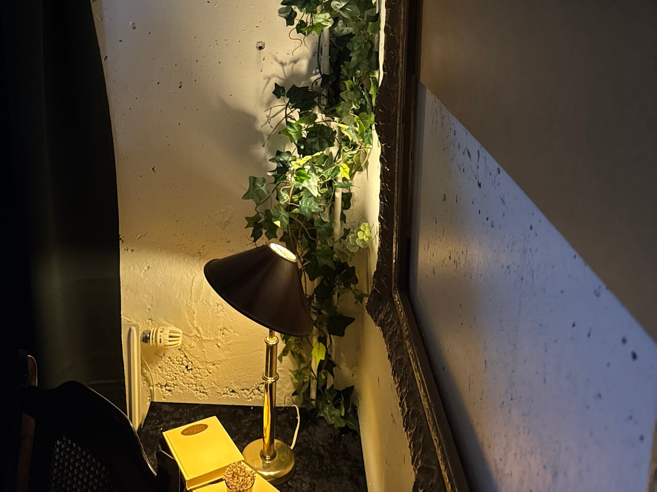 Tänd bordslampa, murgröna och en guldramad tavla i skyddsrummets hörn